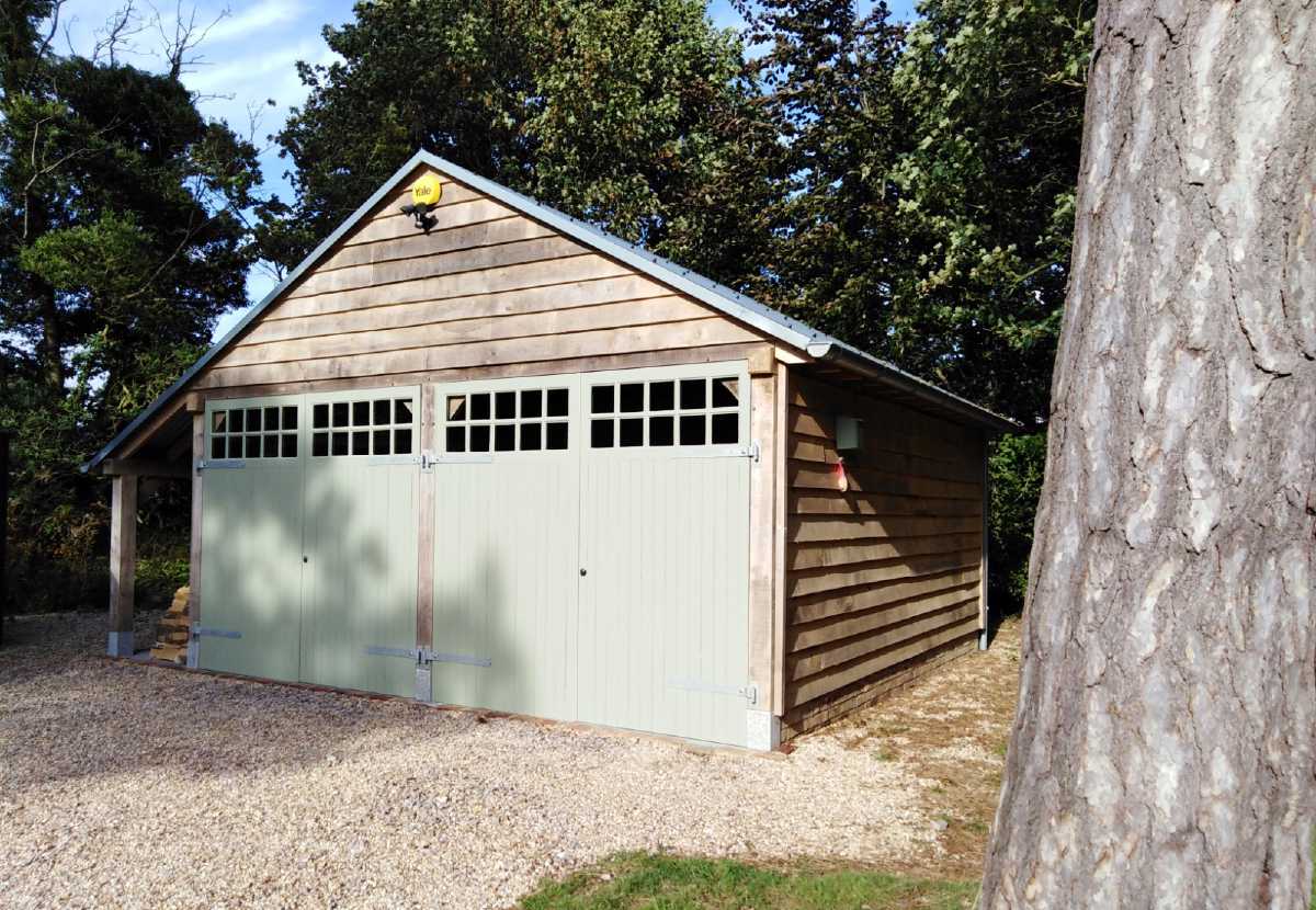 Traditional style oak garage with quarter glazed timber garage doors, fitted with galvanised ironmongery and painted in a complementary heritage colour